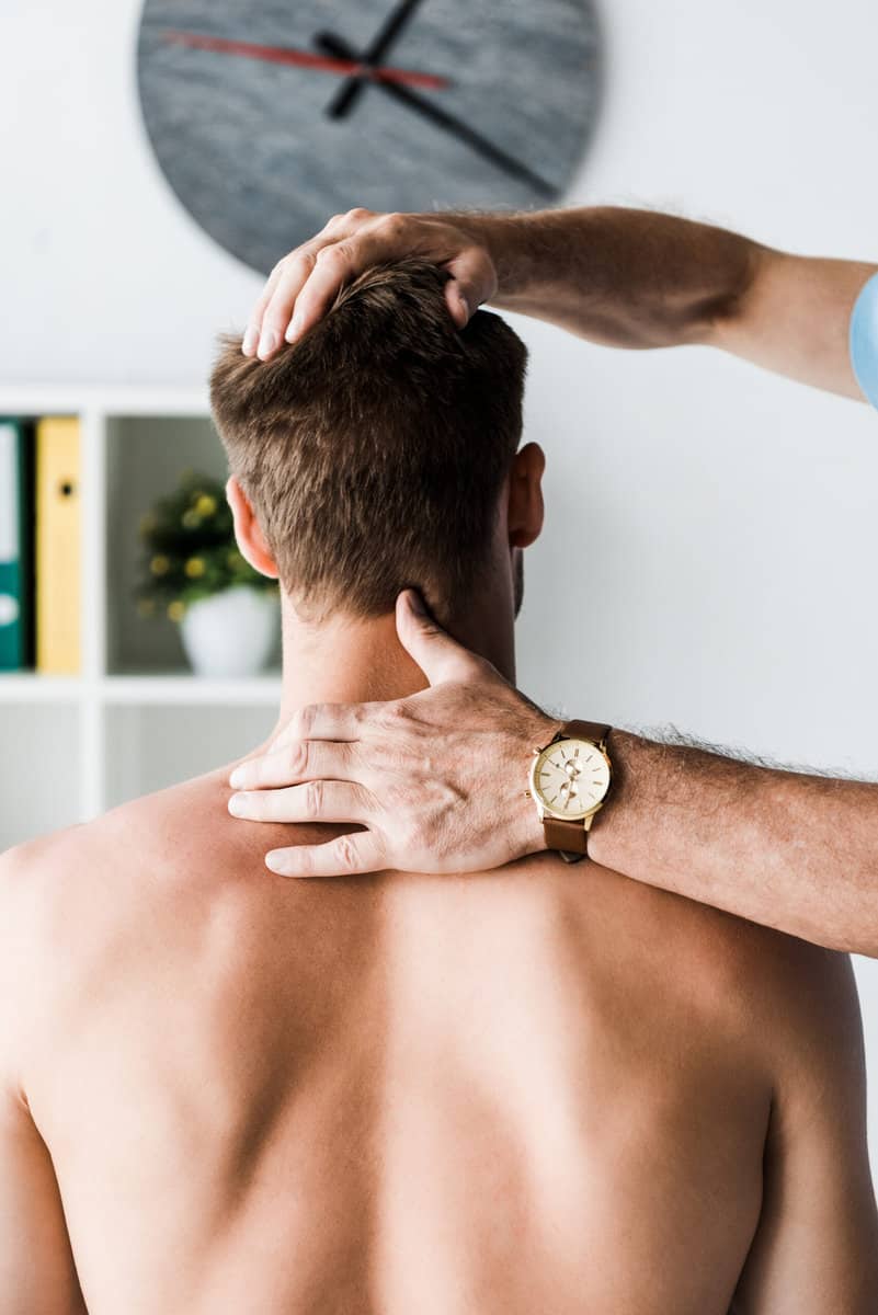 cropped view of doctor touching neck of muscular patient sitting in clinic